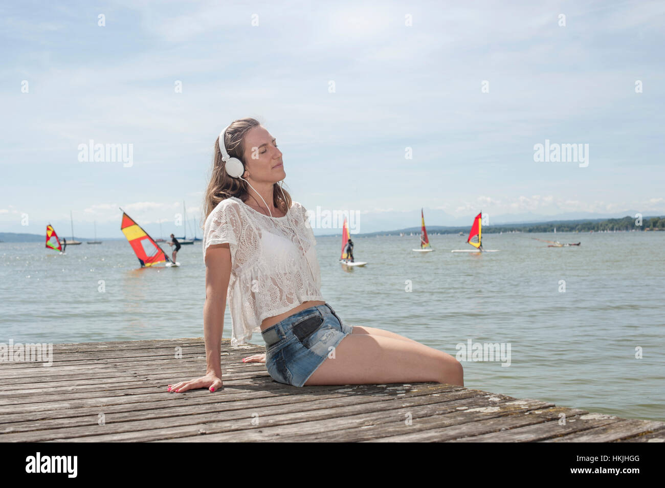 Frau, Musikhören und sitzen auf der Promenade am See, Ammersee, Oberbayern, Deutschland Stockfoto