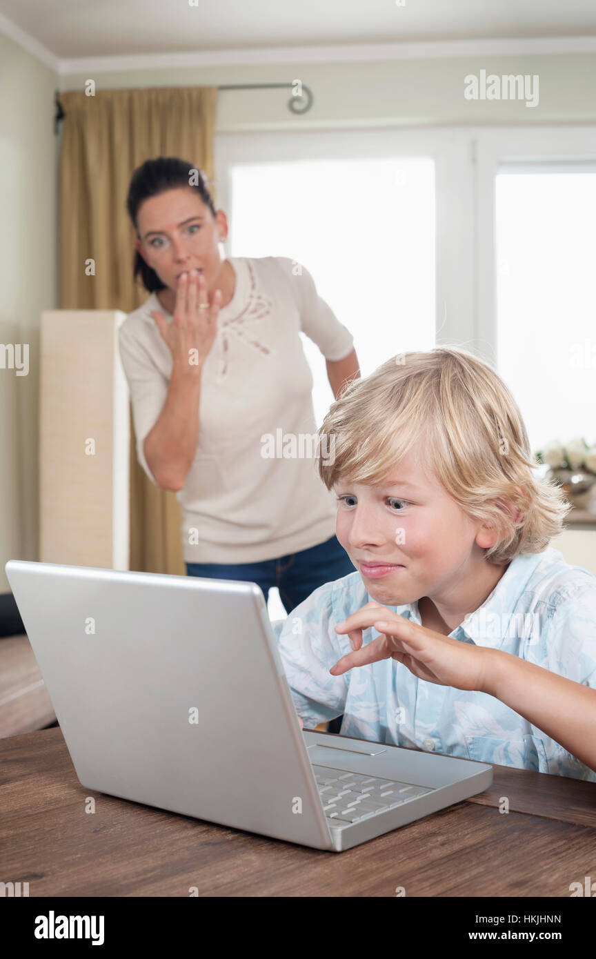 Schockiert Frau, die gerade ihren Sohn mit Laptop im Wohnzimmer, Bayern, Deutschland Stockfoto