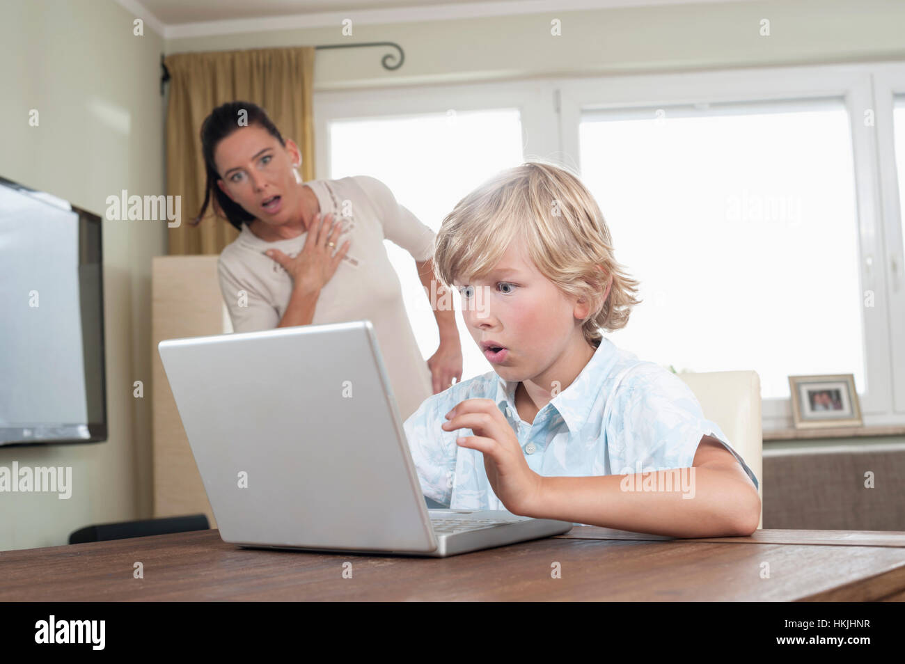 Schockiert Frau, die gerade ihren Sohn mit Laptop im Wohnzimmer, Bayern, Deutschland Stockfoto