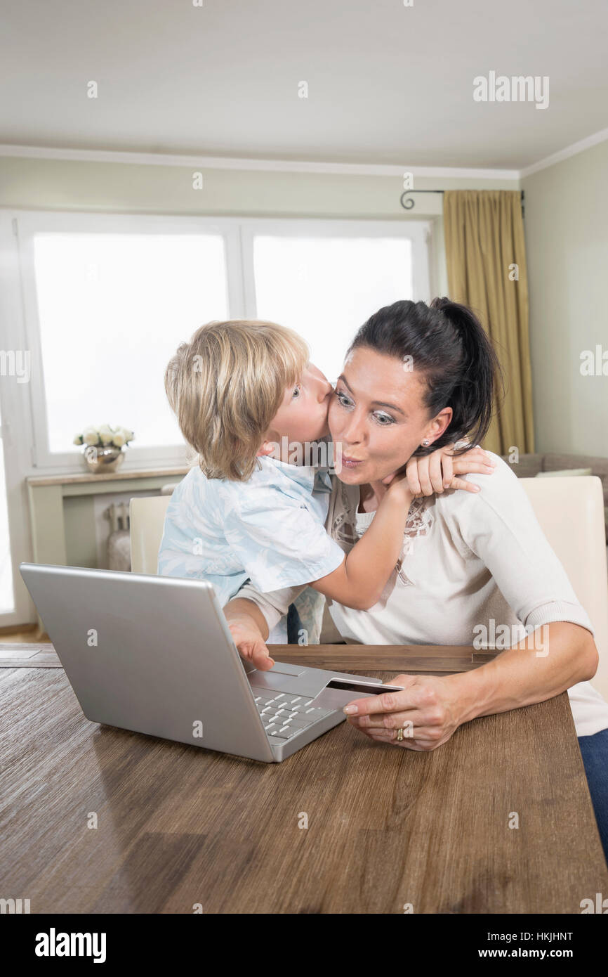 Junge küssen seiner Mutter, während sie online einkaufen auf Laptop, Bayern, Deutschland Stockfoto