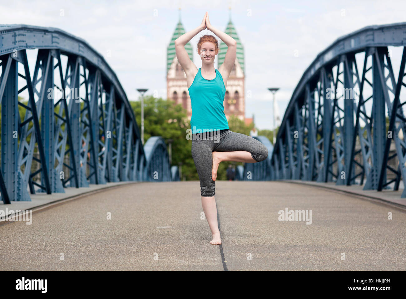Junge Frau beim Baum Pose Yoga auf Brücke in Großstadt, Freiburg Im Breisgau, Baden-Württemberg, Deutschland Stockfoto