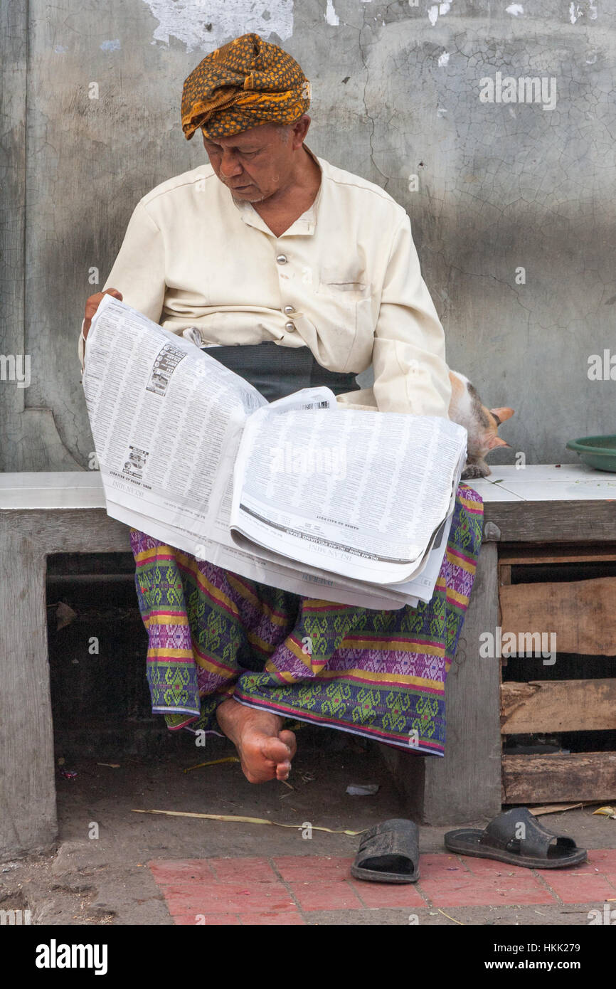 Mann saß auf einer Steinbank, lesen eine Zeitung in Denpasar, Bali, Indonesien Stockfoto