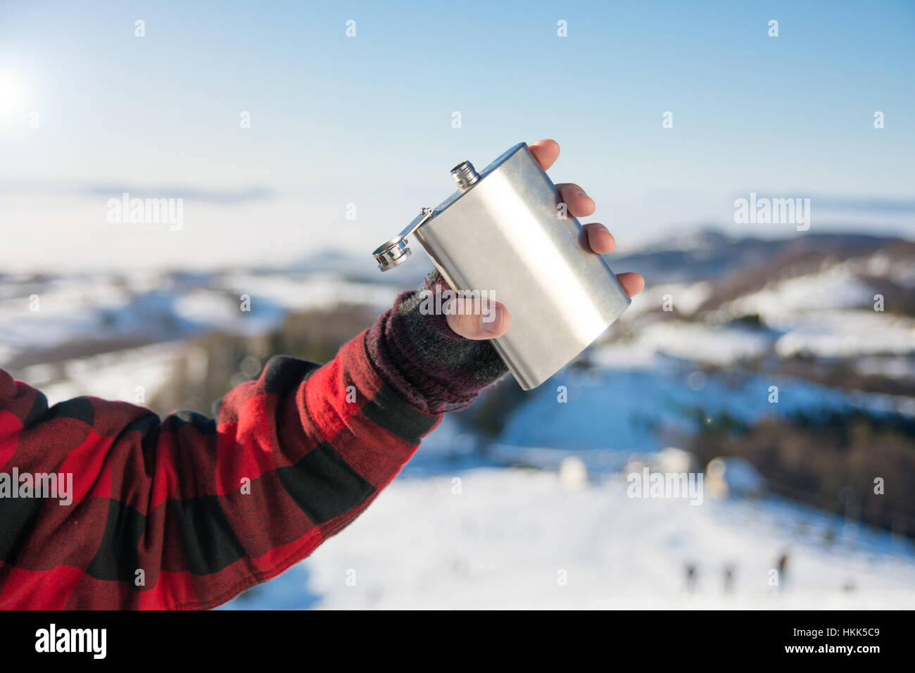 Männliche Hand, die Flachmann auf einem verschneiten Berggipfel Stockfoto