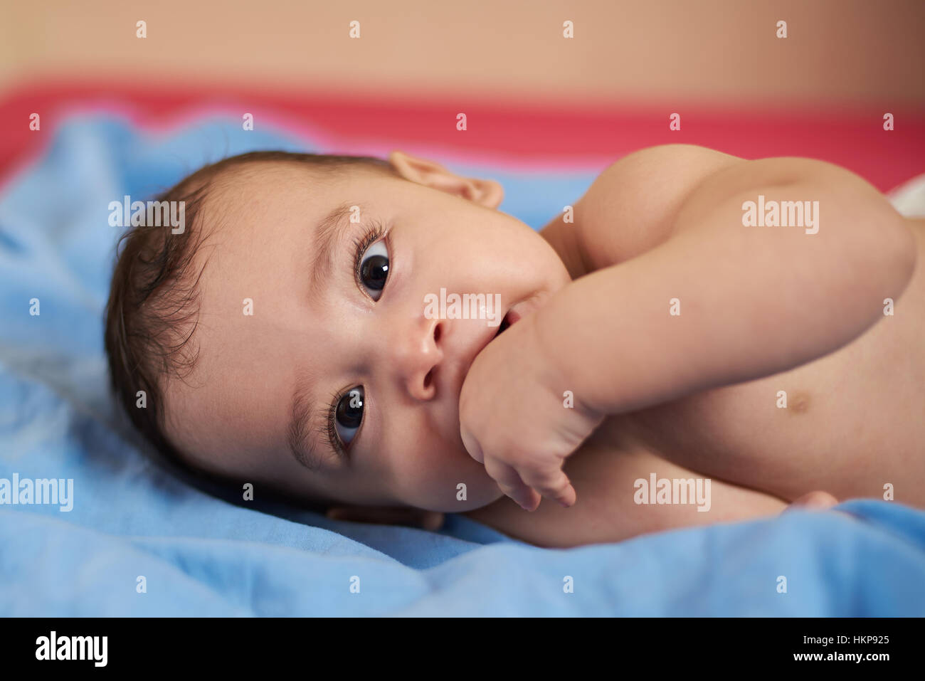 kleine Baby Portrait auf Bett mit Finger im Mund Stockfoto
