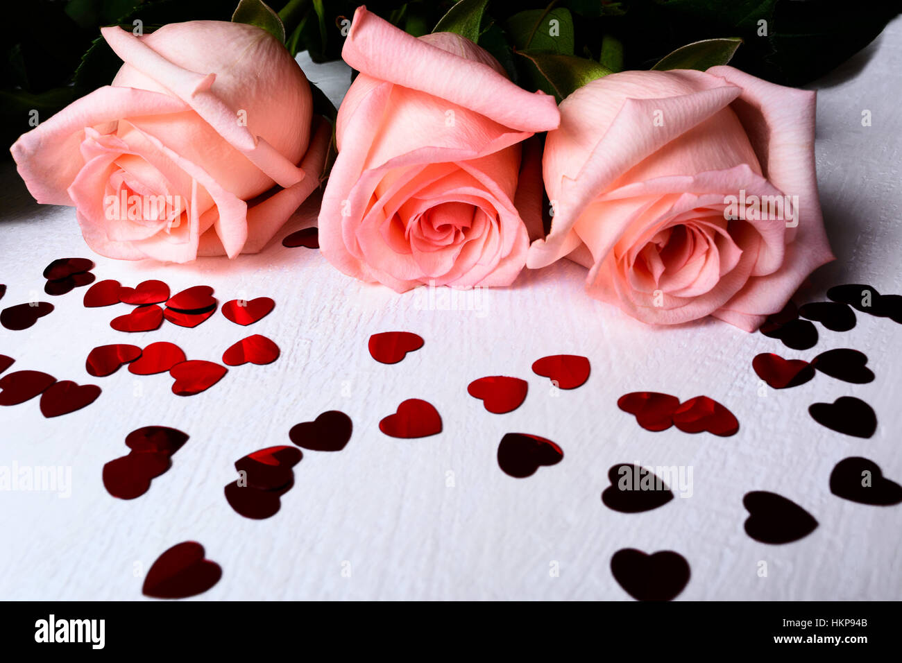 Drei Rosa Rosen mit roten Herzen Formen Pailettes. St. Valentinstag Symbole Hintergrund. Elegante Hochzeit Tag Grußkarte oder Einladung. Stockfoto
