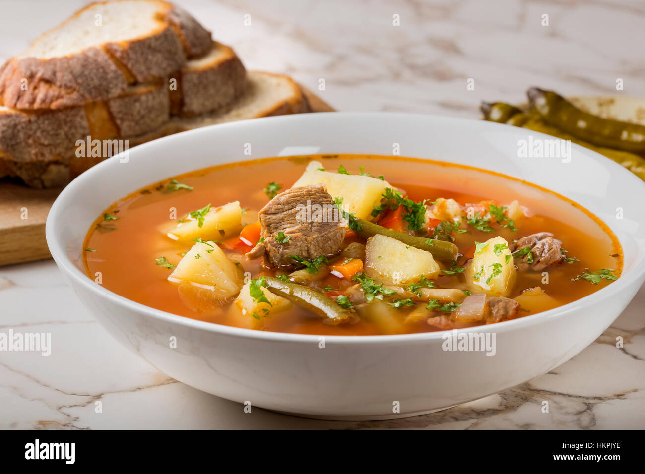 Gemüse Rindfleisch Suppe mit geschnittenem Brot und hot chili Peppers im Hintergrund Stockfoto