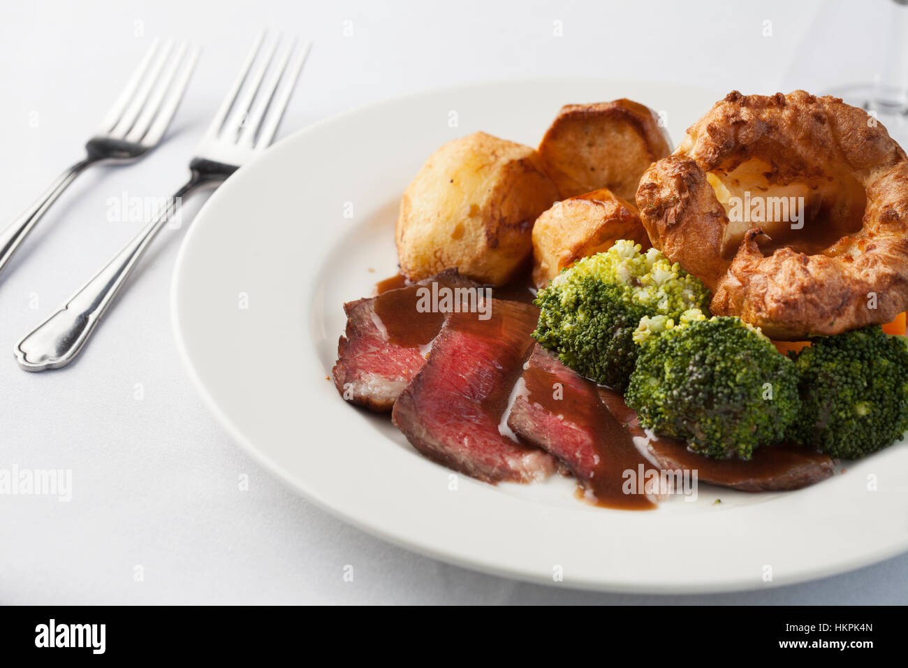 Traditionelle britische Braten Abendessen seltene Rindfleisch, Yorkshire Pudding, Bratkartoffeln und Brokkoli mit Sauce. Stockfoto