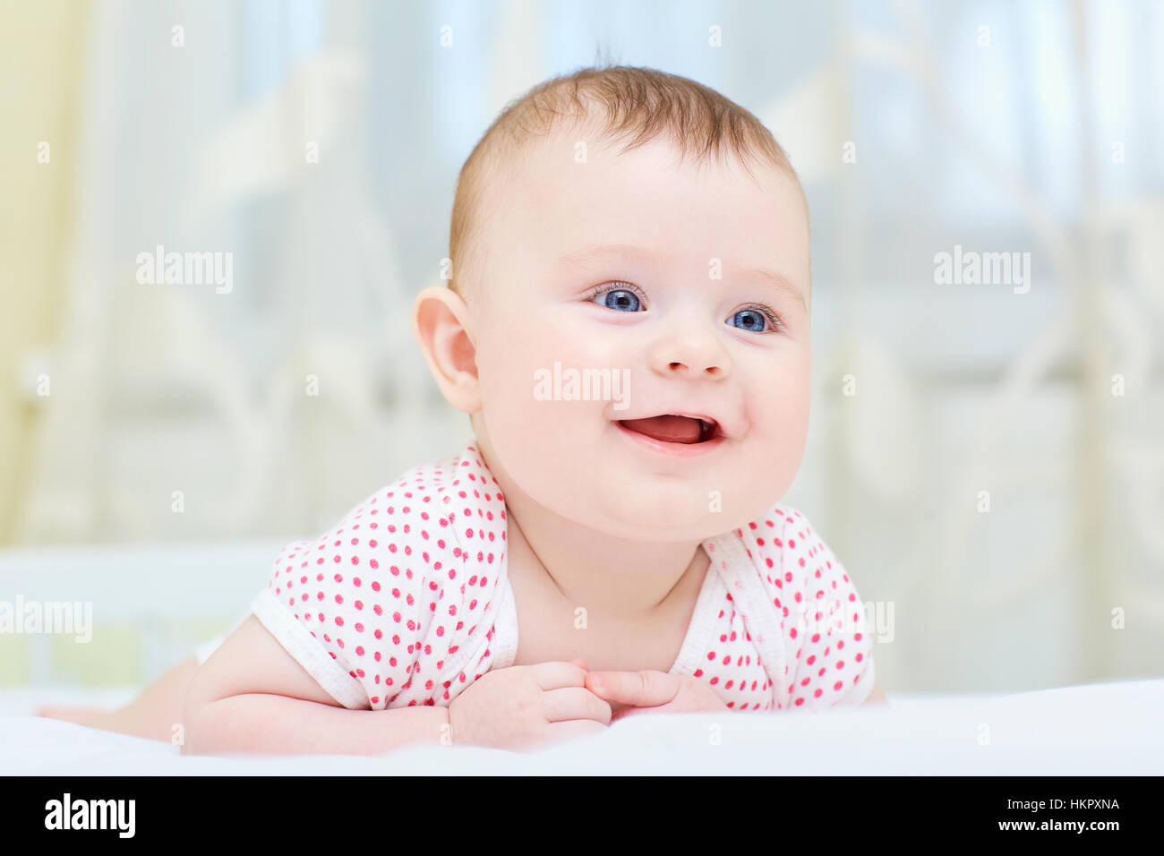 Baby, Kleinkind lächelnd auf einem weißen Bett liegend Stockfoto