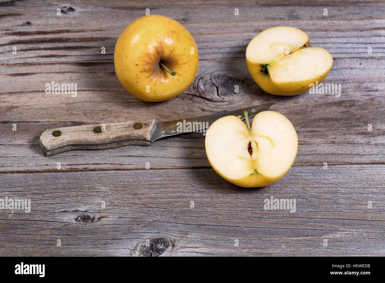 Selektiven Fokus auf geschnittene Goldener Apfel mit Schälmesser und ganze Apple im Hintergrund auf urigen Holzbrettern Stockfoto