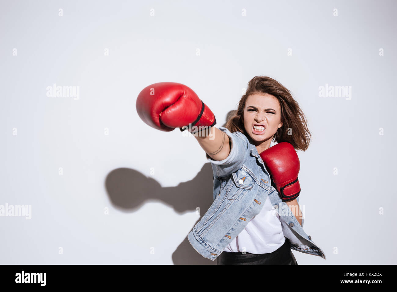 Foto von Boxer wütend Frau gekleidet in Jeansjacke und Handschuhe machen Boxen Übung isoliert auf weißem Hintergrund Stockfoto