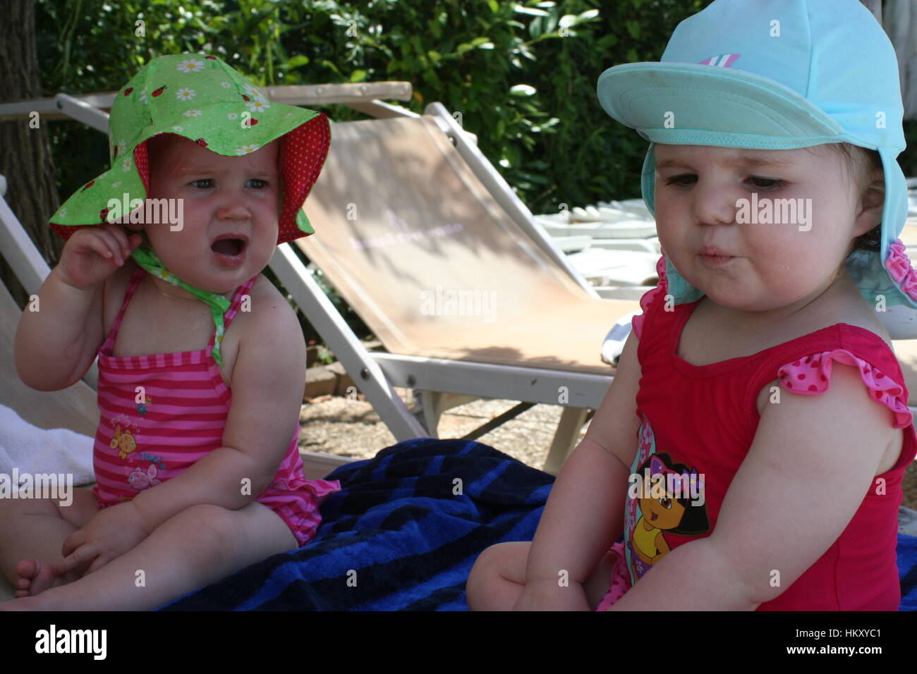 Lustiges Foto von Baby Mädchen, Badeanzüge und sun Hüte sitzen im Sommer Sonne unglücklich, lustige Kinder Konzept Kinder suchen Stockfoto
