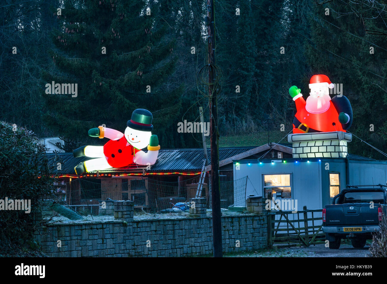 Riesige beleuchtete aufblasbare Weihnachtsfiguren umgeben eine abgelegene Hütte in der Nacht in ländlichen Herefordshire, England. Stockfoto