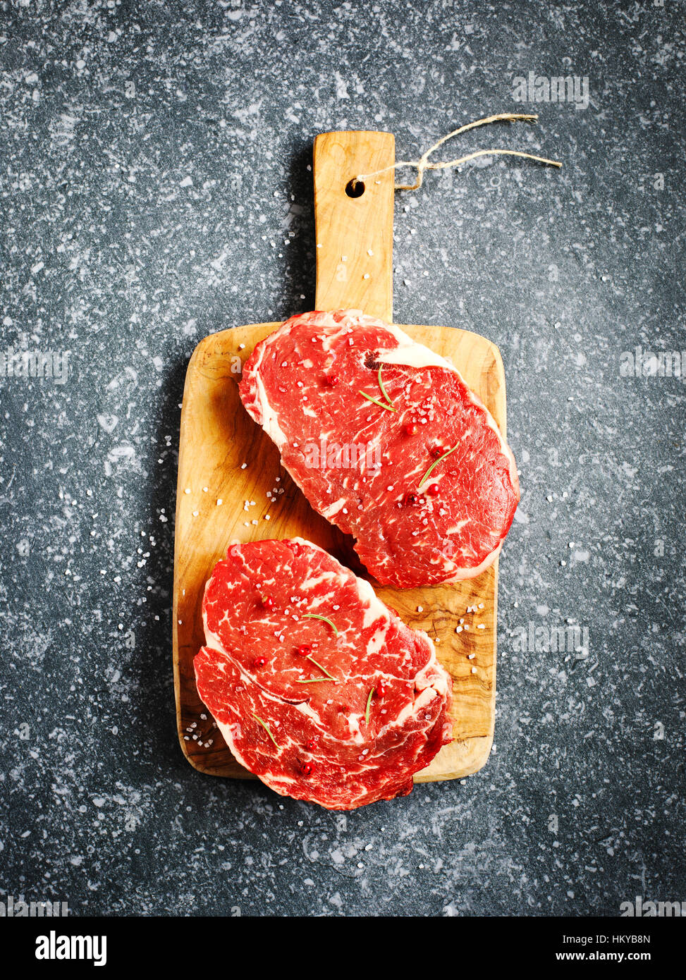 Rohes Frischfleisch Ribeye Steak mit Rosmarin, Pfeffer und Meersalz auf Stein Schiefer Hintergrund Stockfoto