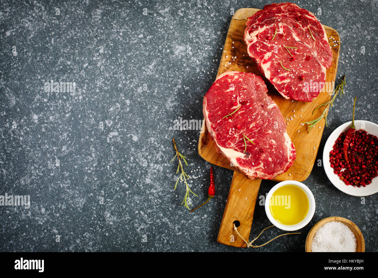 Rohes Frischfleisch Ribeye Steak mit Rosmarin, Pfeffer, Salz und Olivenöl auf Stein Schiefer Hintergrund Stockfoto