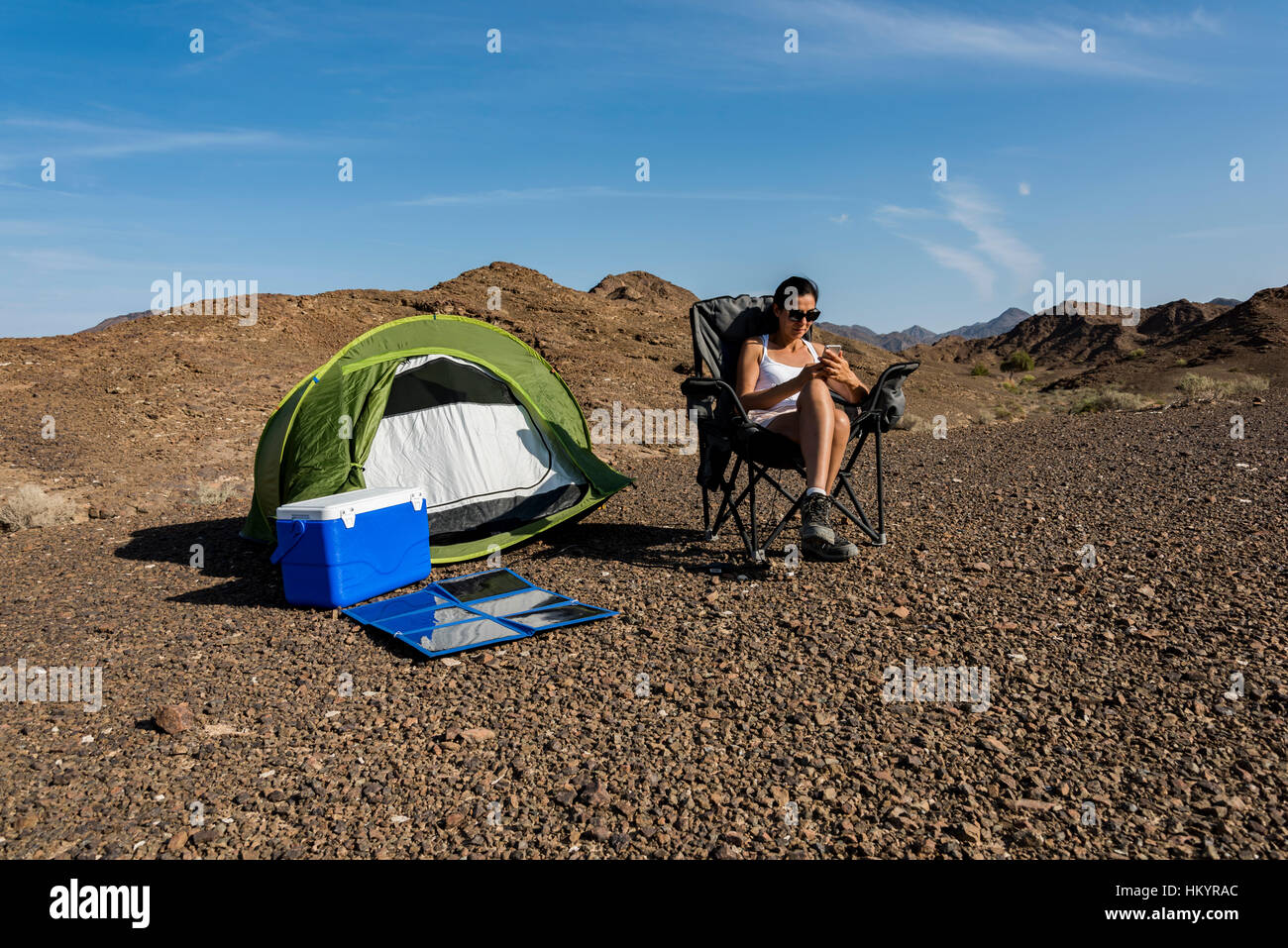Frau in den Bergen mit ihrem Smartphone zu spielen, während des Ladevorgangs mit einem faltbaren Solarpanel. Stockfoto