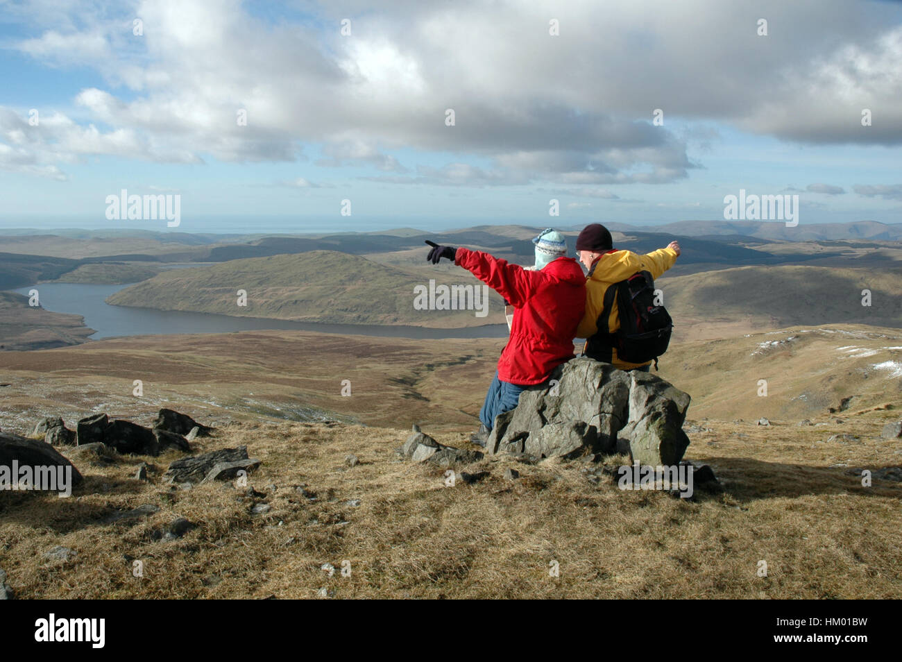 Zwei Hügel Wanderer auf Felsen am Gipfel Karte lesen und zeigen in entgegengesetzte Richtungen, hellen Wintertag mit See unten sitzen Stockfoto