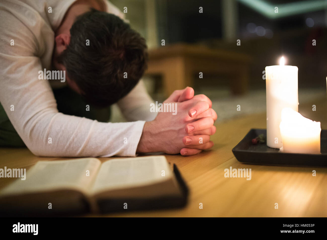 Junger Mann beten, kniend, Bibel und Kerze neben ihm. Stockfoto