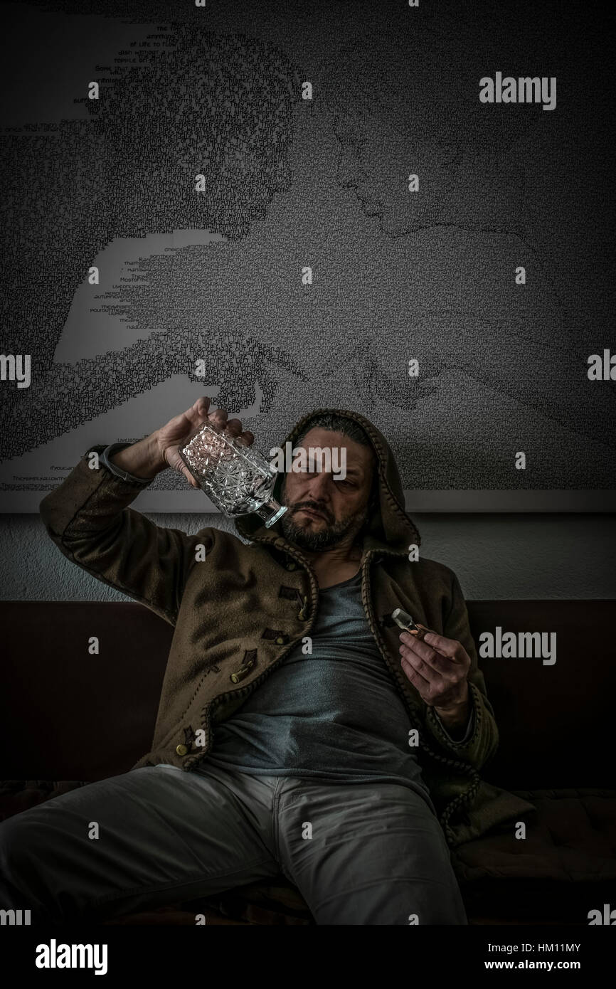 Ein Mann mit einer Kapuze sitzt, hält mit seiner Hand eine leere Glasflasche mit Alkohol graviert und schaut enttäuscht auf sie Stockfoto
