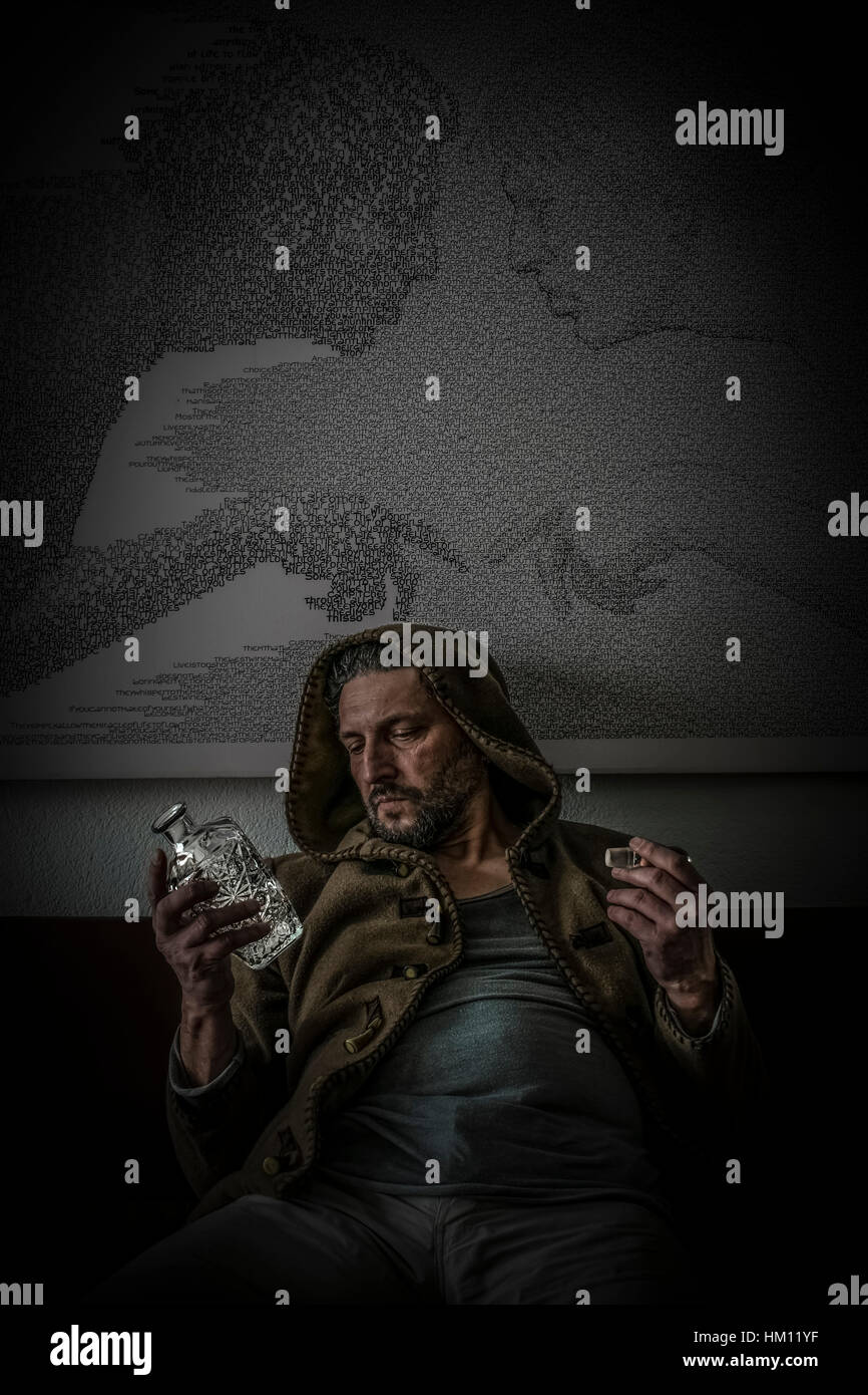 Ein Mann mit einer Kapuze sitzt, hält mit seiner Hand eine leere Glasflasche mit Alkohol graviert und schaut enttäuscht auf sie Stockfoto