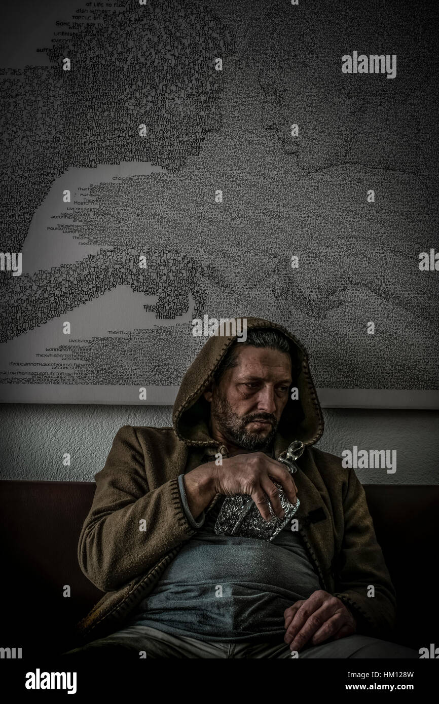 Ein Mann mit einer Kapuze auf sitzen und mit seiner Hand eine leere gravierte Glasflasche Alkohol und Blick nach unten in Enttäuschung. Stockfoto