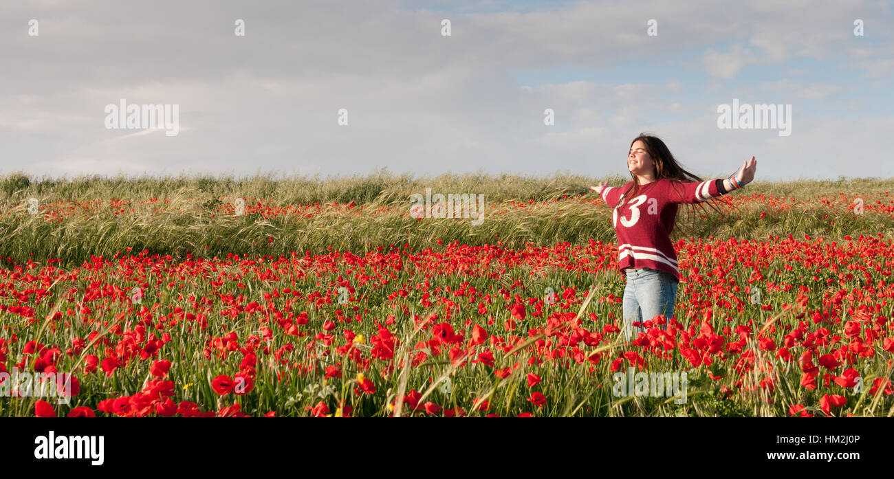 Glücklich schöne Teenager-Mädchen stehen im roten Feld von Mohn, genießen Sie die wunderschöne Landschaft und frei zu fühlen. Stockfoto