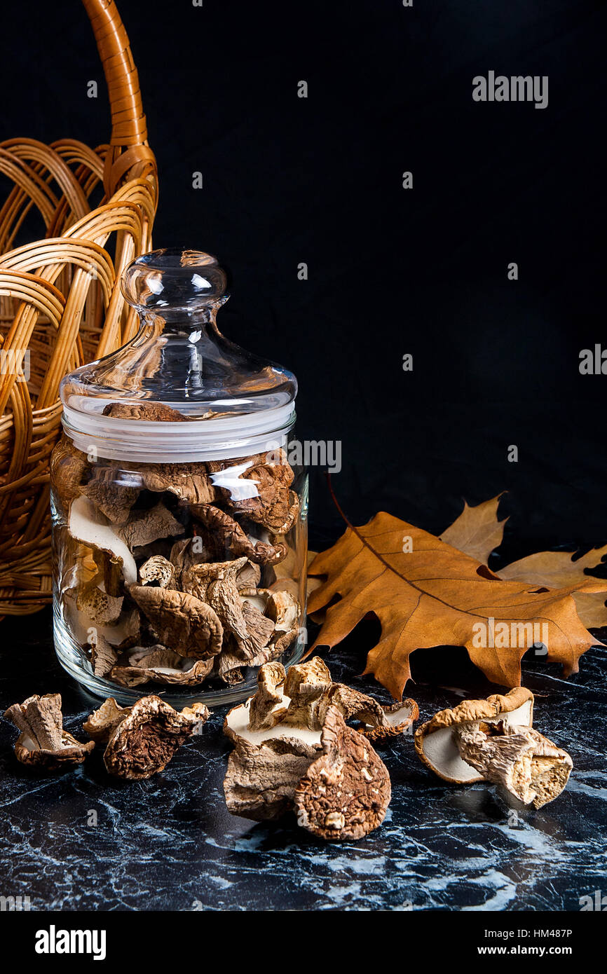 Trockene weiße Pilze im Glas und auf den Tisch. Gelb aus Holz Korb am hinteren Hintergrund und mehrere trockenes Eichenlaub. Stockfoto