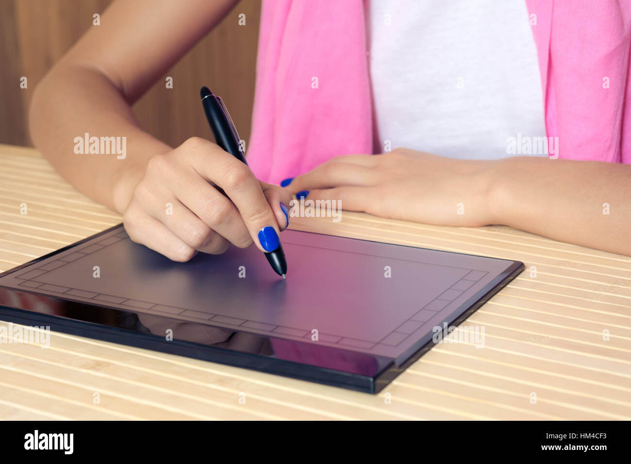 Frau in rosa Schal und blauem Maniküre stützt sich auf das Tablet an einen Holztisch Nahaufnahme. Stockfoto