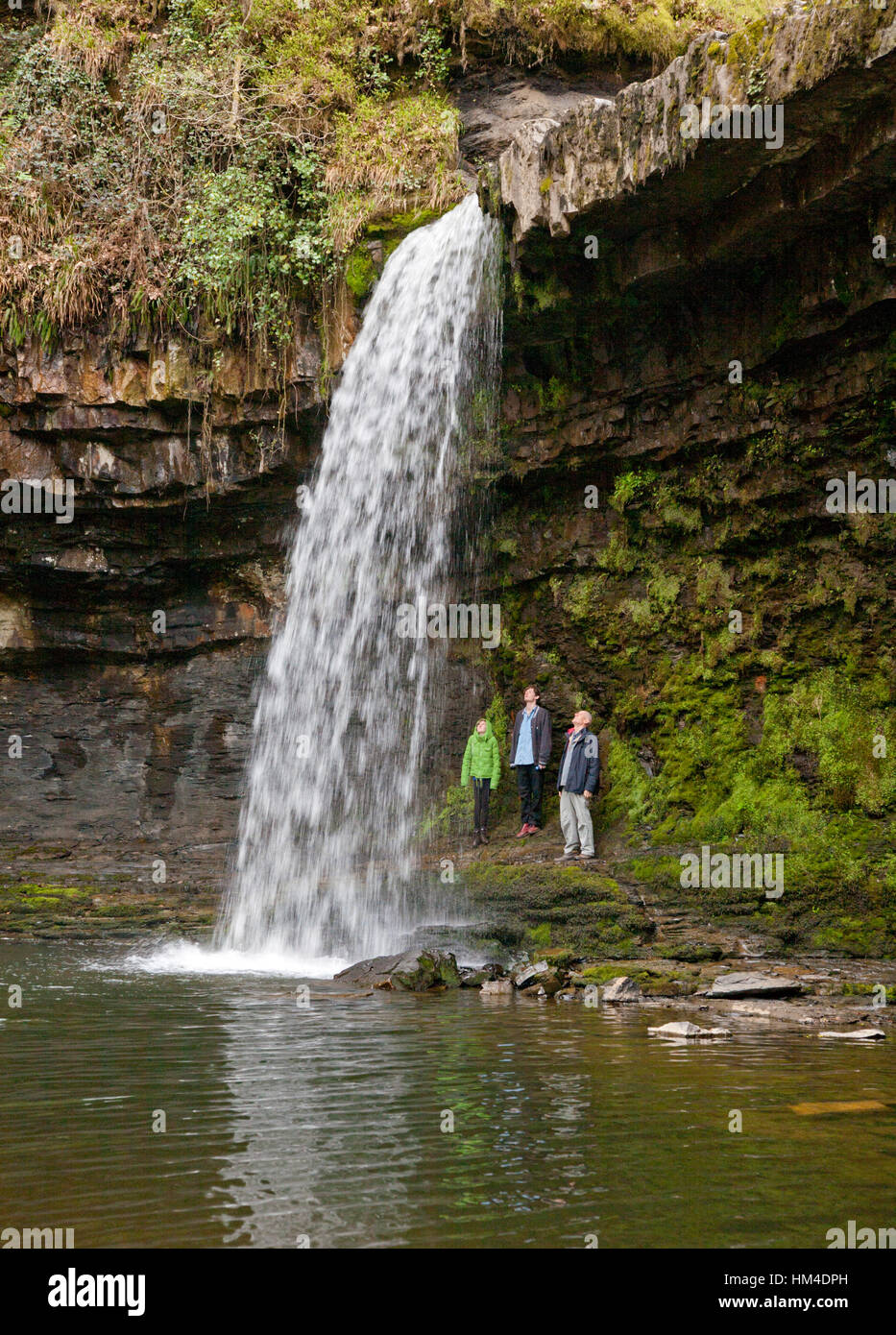 Wanderern stehen hinter dem Sgwd Gwladus Wasserfall in der Nähe von Ystradfellte in Brecons, Wales. Stockfoto