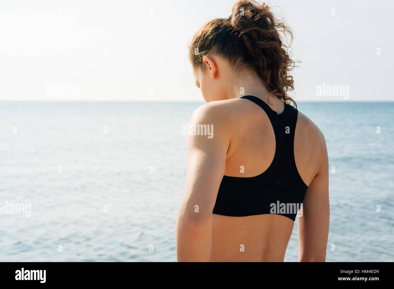 Sportliche Mädchen mit lockigen Haaren in einen Sport-BH am Ufer stehen und  Blick auf das Wasser bei Sonnenaufgang, Ansicht von hinten Stockfotografie  - Alamy
