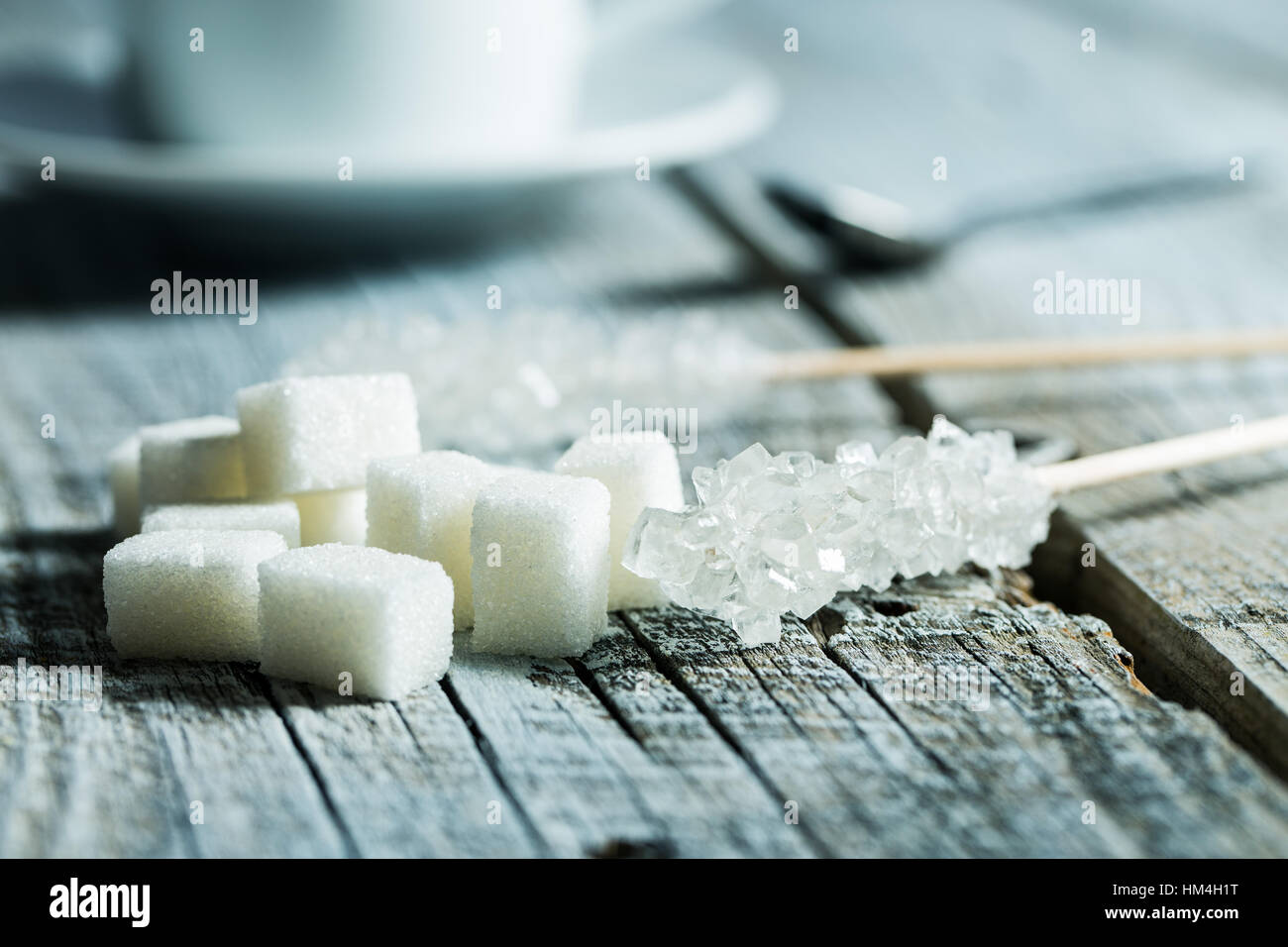 Kristallisierter Zucker auf Holzstab und Zuckerwürfel auf Holztisch. Stockfoto