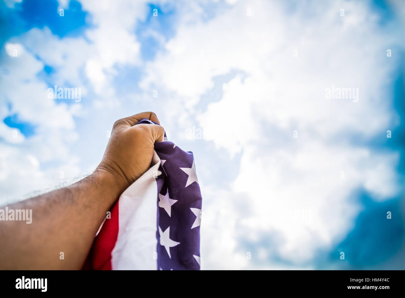 Amerikanische Flagge mit Sternen und Streifen halten mit Händen gegen blauen Himmel Stockfoto