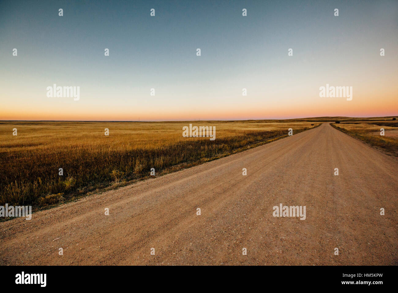 Leere unbefestigte Straße inmitten von Wiese gegen klaren Himmel bei Sonnenuntergang Stockfoto
