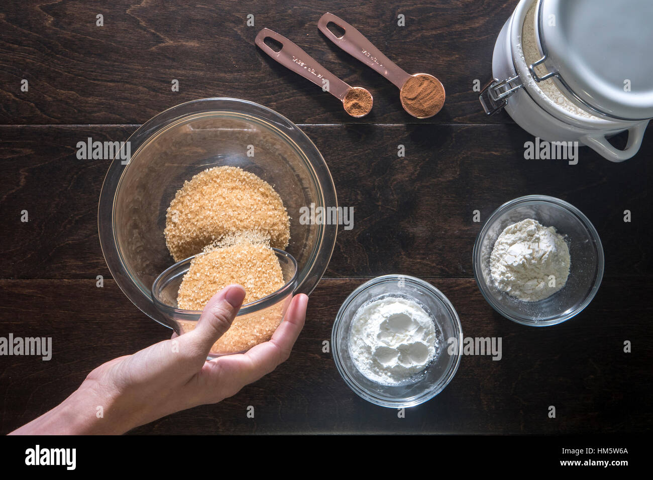 Bild der Frau Gießen brauner Zucker in die Schüssel auf Holztisch beschnitten Stockfoto