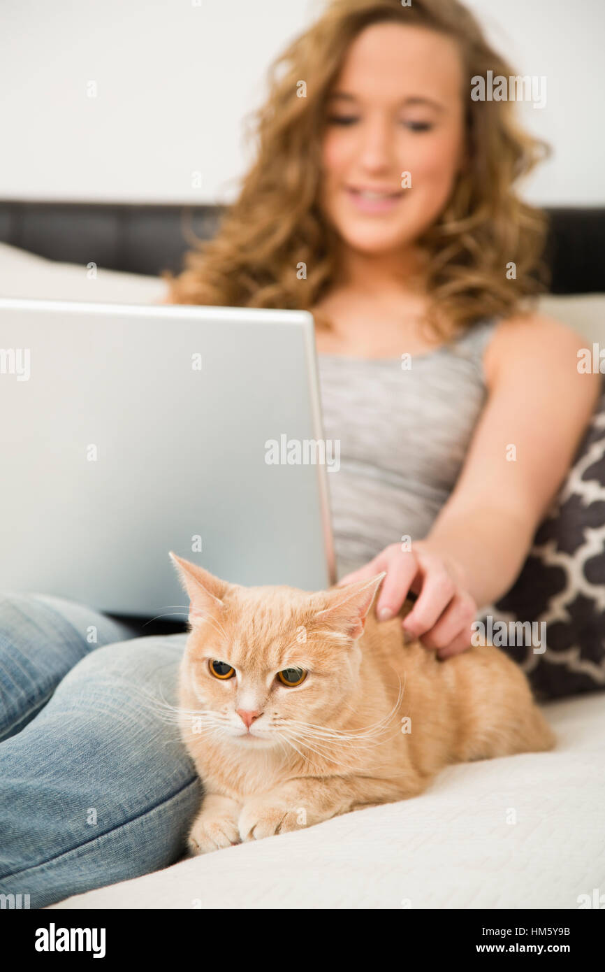 Teenager-Mädchen (16-17) auf Bett mit Laptop und streichelte Ingwer Tabby Katze liegend Stockfoto