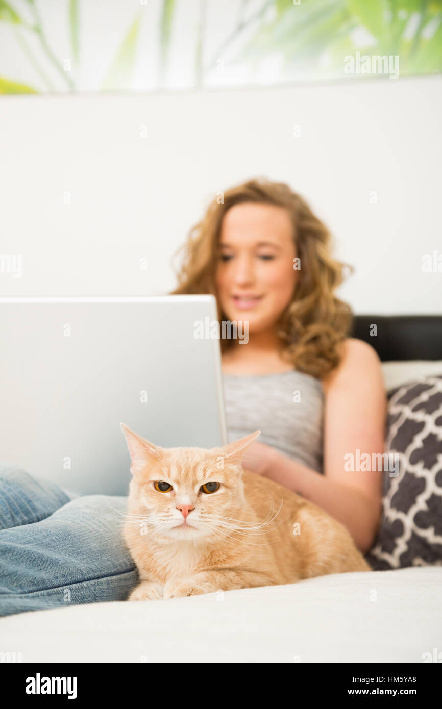 Teenager-Mädchen (16-17) auf Bett liegend mit Laptop und Ingwer Tabby Katze Stockfoto
