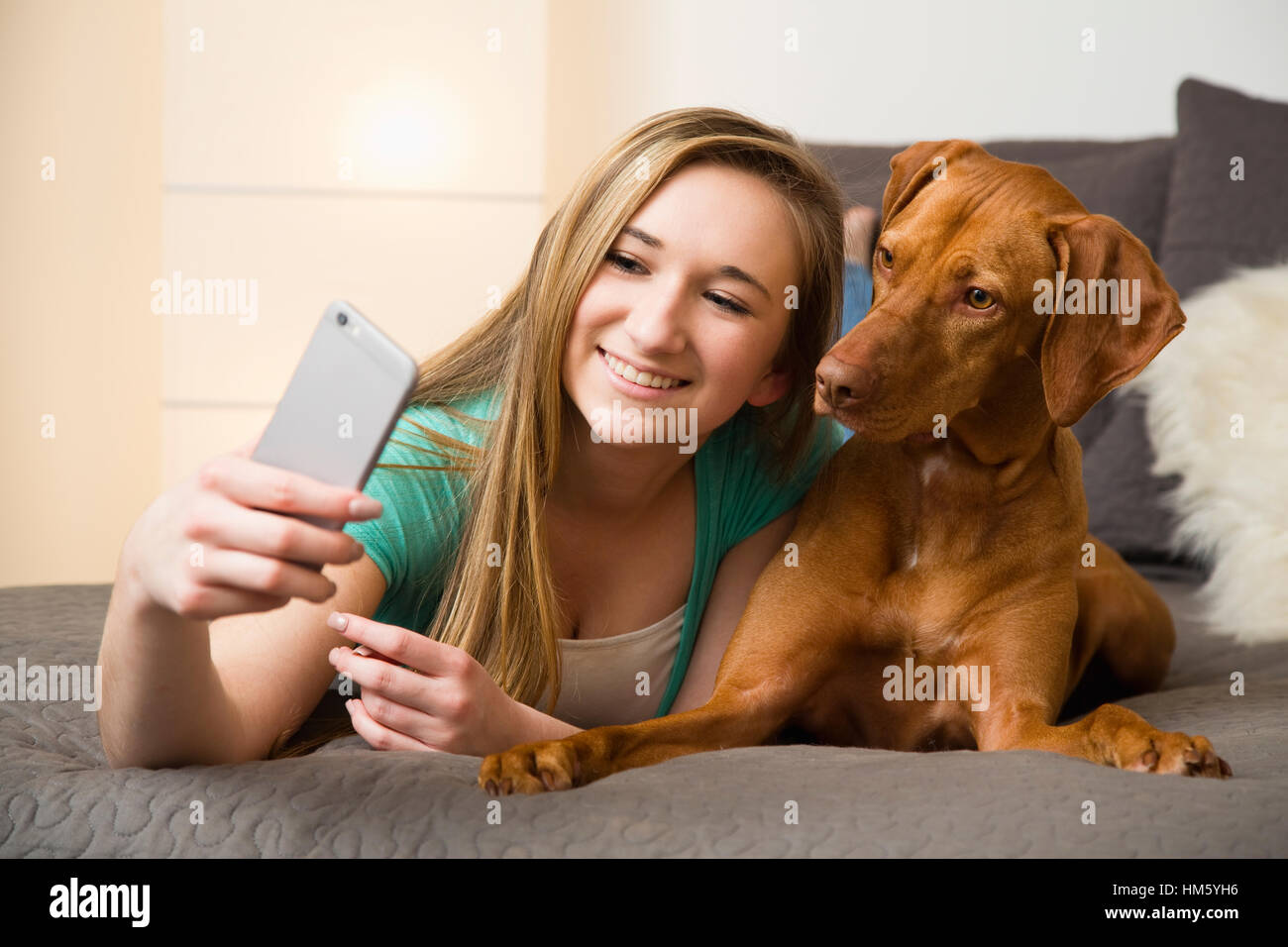 Teenager-Mädchen (16-17) auf Bett liegend mit brauner Vizsla Hund und nehmen selfie Stockfoto