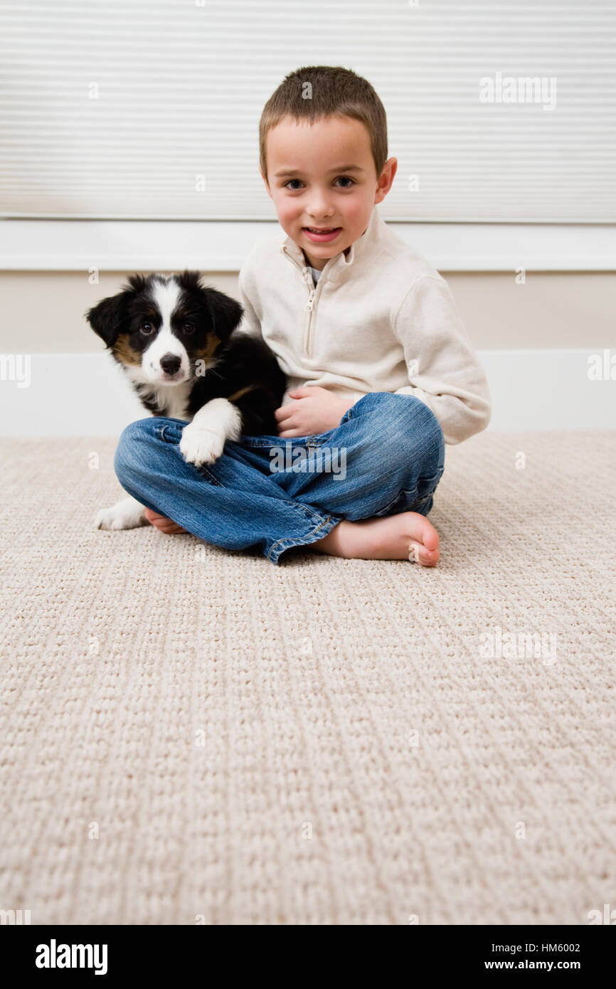 Junge sitzt mit Welpen auf Teppich Stockfoto