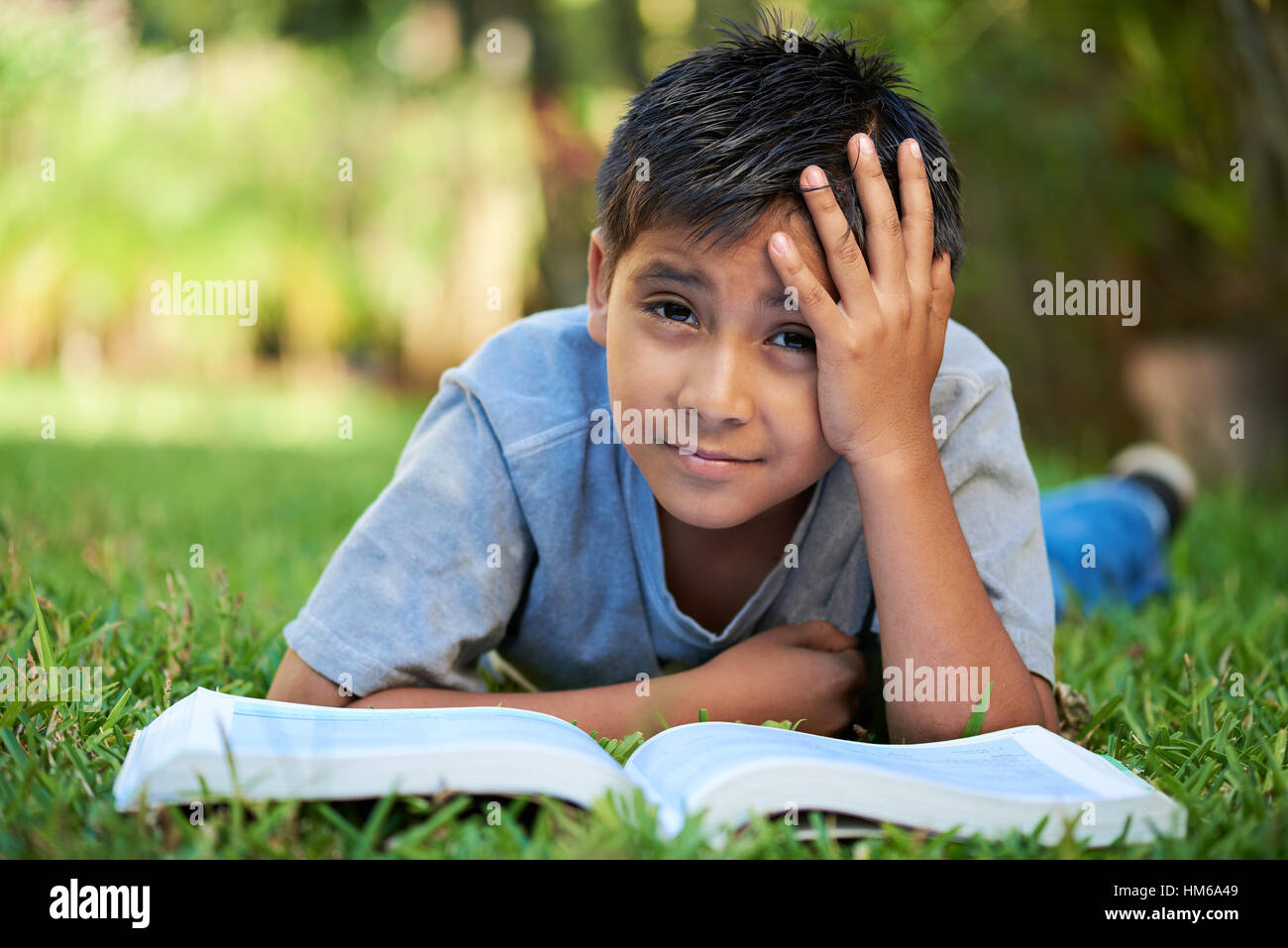 kleiner Junge mit Buch gelangweilt lag auf dem grünen Rasen Stockfoto