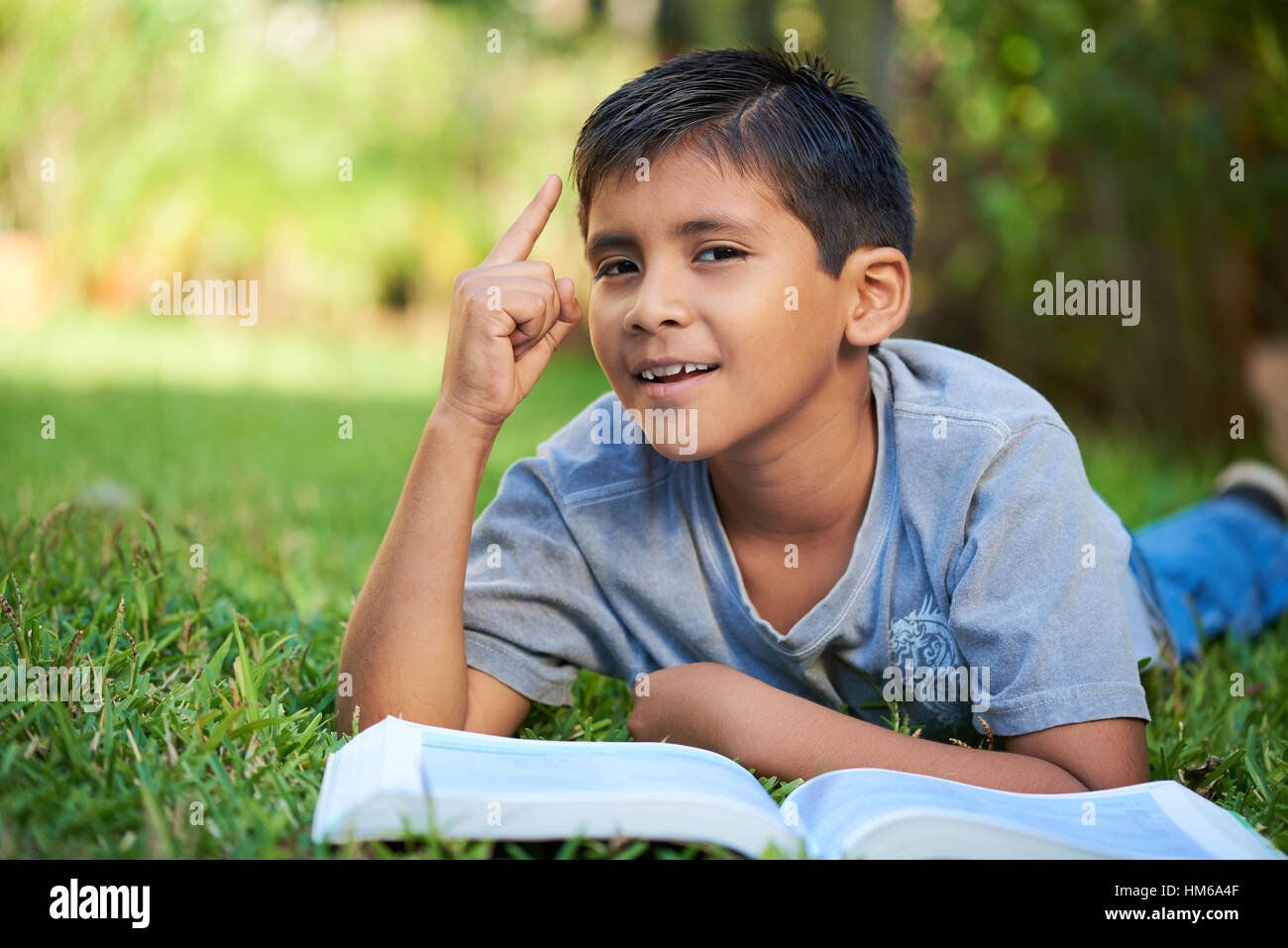 kleiner Junge bekam Idee lag mit Buch in Rasen Stockfoto