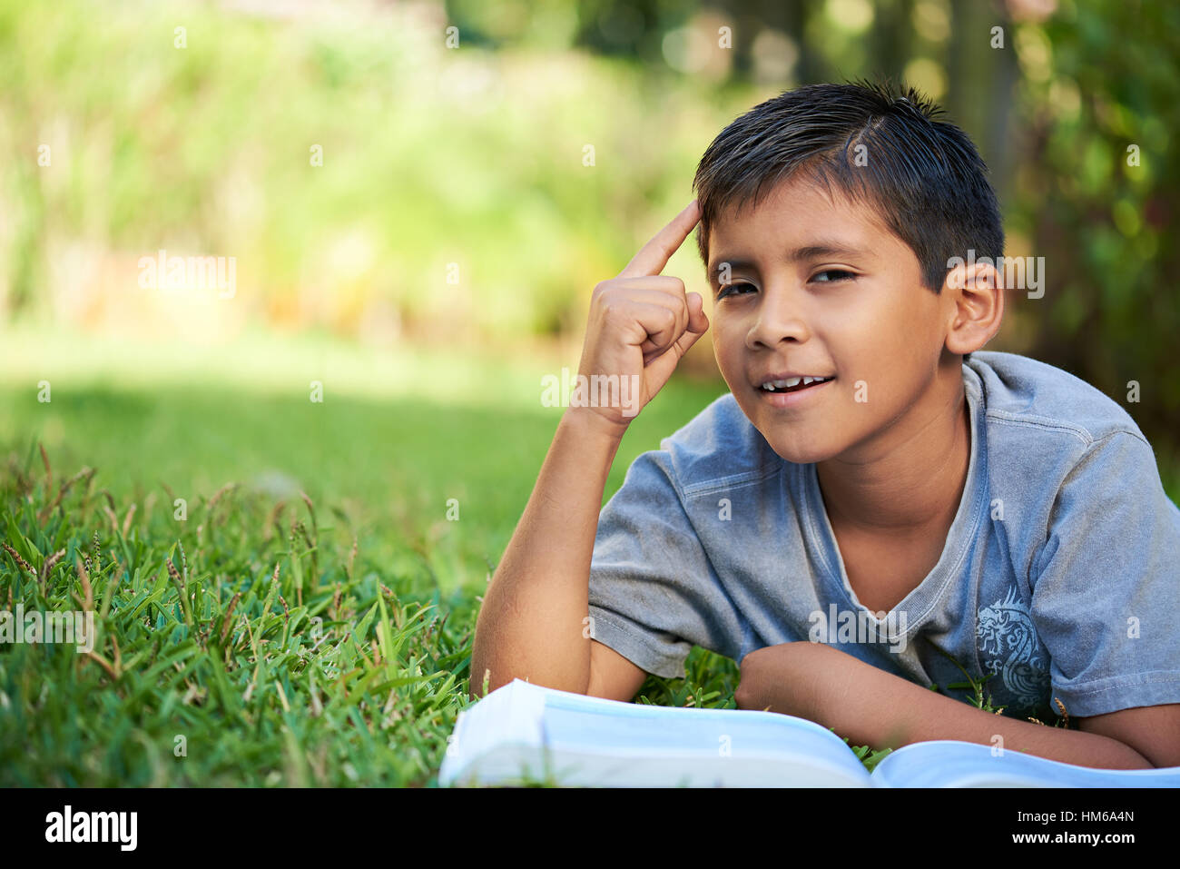 kleiner Junge aus Buch auf dem grünen Rasen im Park lernen Stockfoto
