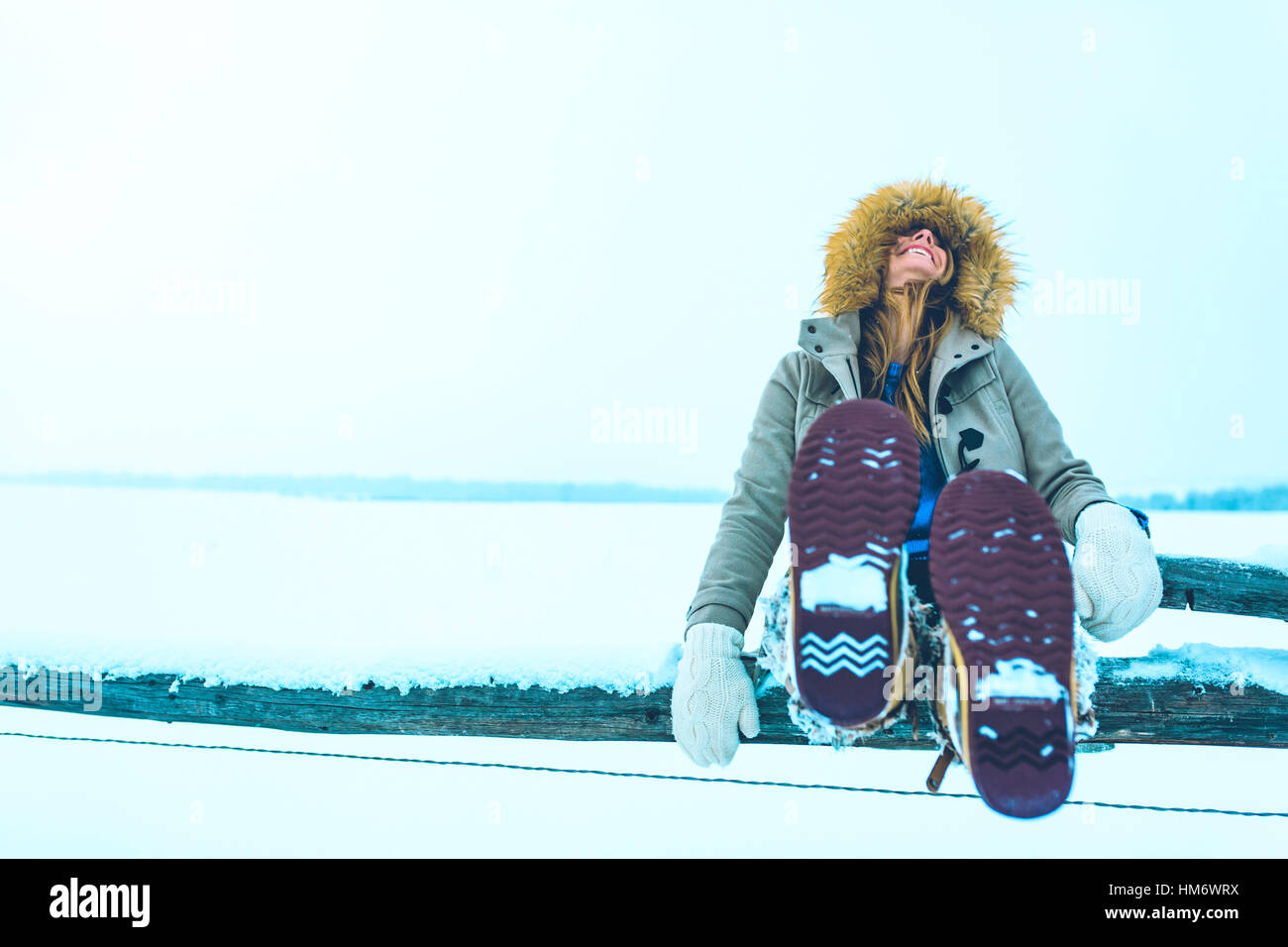 Stets gut gelaunte Frau sitzen auf Geländer an Schnee bedeckt Feld Stockfoto