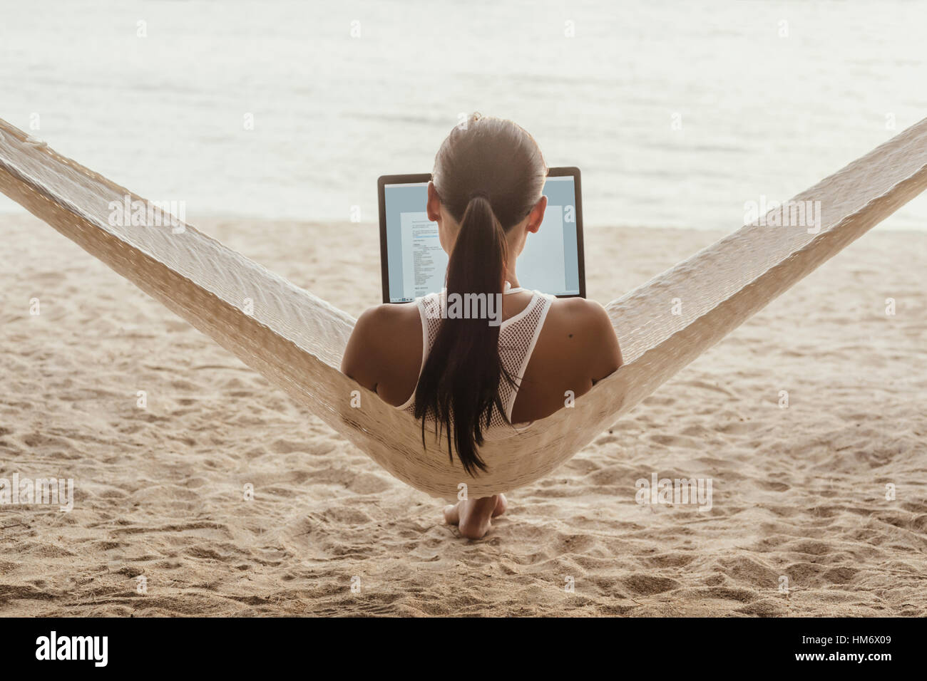 Rückansicht des Frau mit Laptop-Computer beim Entspannen auf der Hängematte Stockfoto