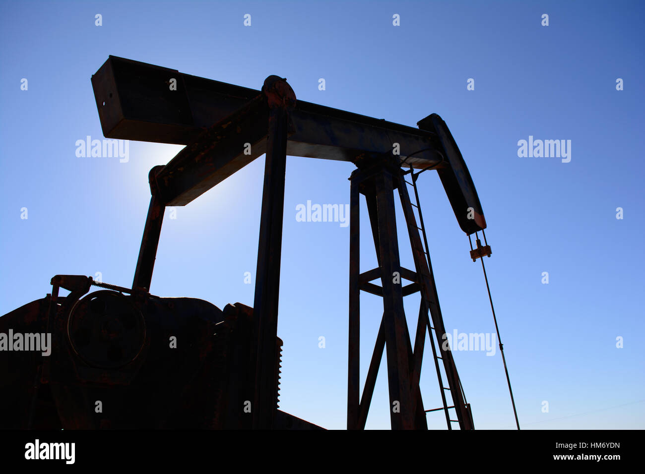 Ölfeld Bohrschwengels, rostig und alt, Silhouette durch die Sonne. Klarer blauer Himmelshintergrund. Zeigt Ölfeld Leben, Erdölindustrie und fossile Brennstoffe. Stockfoto