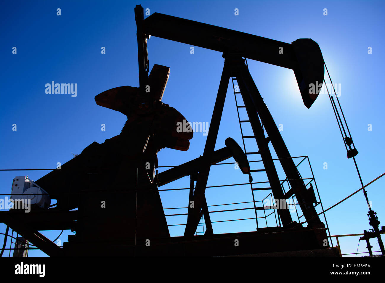 Ölfeld Bohrschwengels, rostig und alt, Silhouette durch die Sonne. Klarer blauer Himmelshintergrund. Zeigt Ölfeld Leben, Erdölindustrie und fossile Brennstoffe. Stockfoto