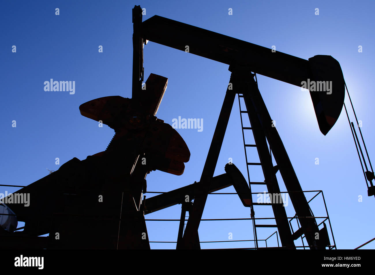 Ölfeld Bohrschwengels, rostig und alt, Silhouette durch die Sonne. Klarer blauer Himmelshintergrund. Zeigt Ölfeld Leben, Erdölindustrie und fossilen Brennstoffen. Stockfoto