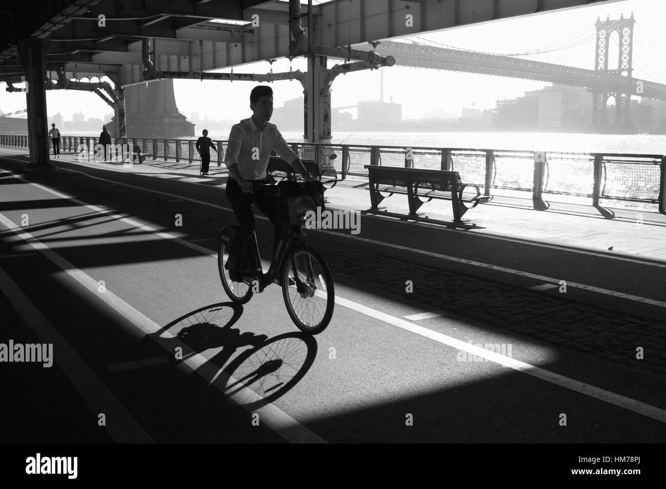 Mann, Radfahren entlang der East River Esplanade unter der Manhattan Brücke bei Sonnenaufgang Monochrom Stockfoto