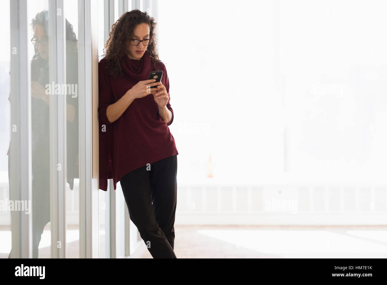Junge Frau stützte sich auf Glaswand und Text-messaging Stockfoto