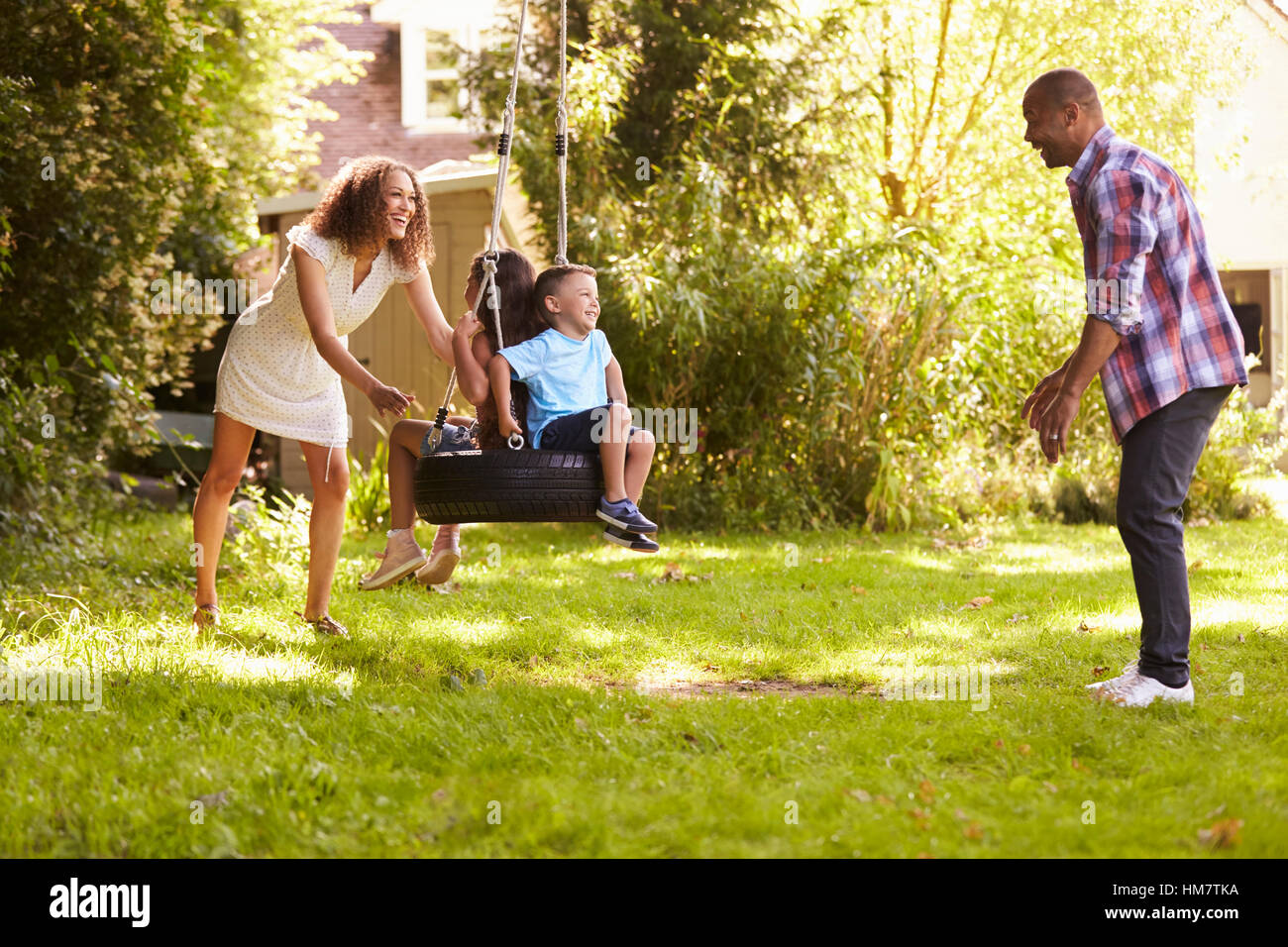 Eltern, die Kinder auf den Reifen schieben Schaukel im Garten Stockfoto