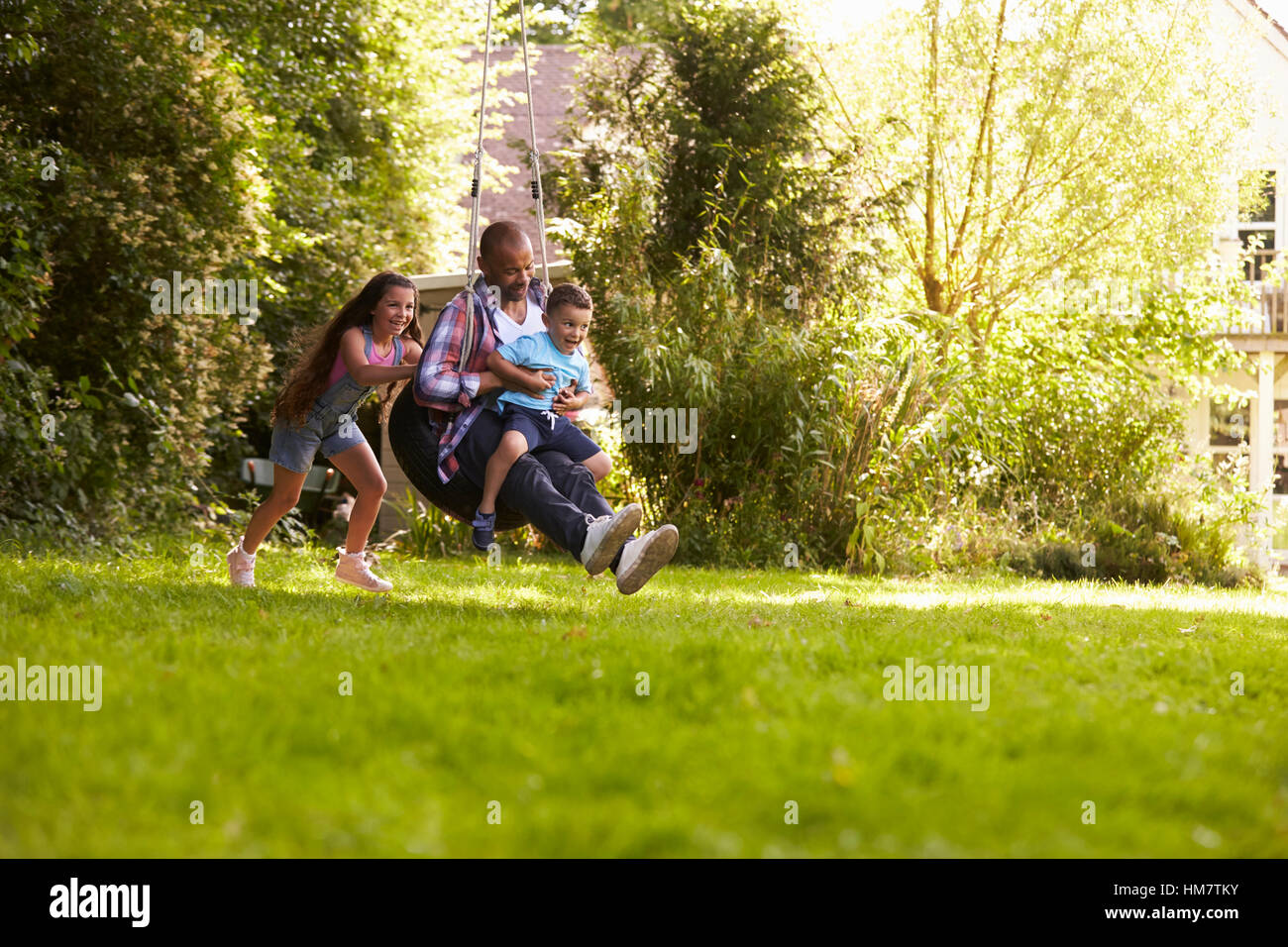 Tochter drängen Vater und Sohn auf Reifen Schaukel im Garten Stockfoto