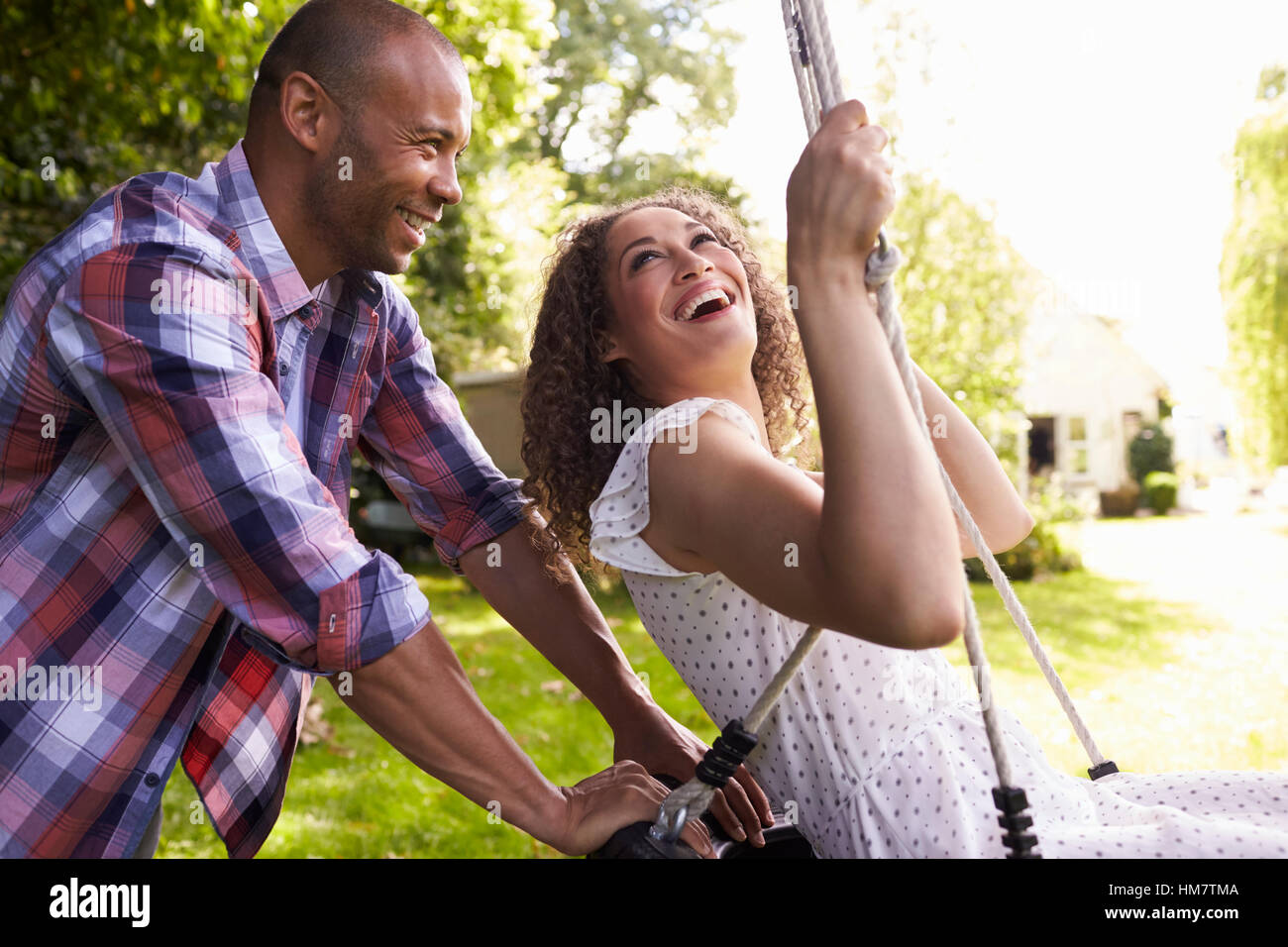 Seitenansicht der Mann schob Frau auf Reifenschaukel im Garten Stockfoto